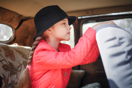Portrait of a cute little girl with a black hat in a retro car.の写真素材