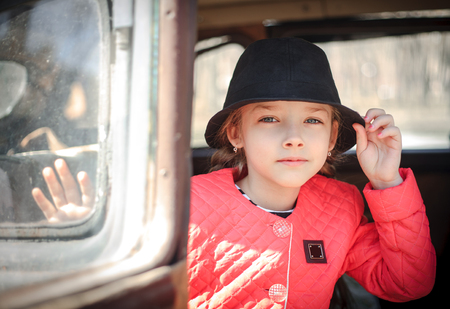 Portrait of a cute little girl with a black hat in a retro car.の写真素材