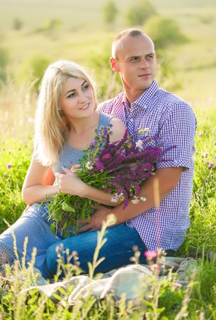 A handsome man and an attractive woman sitting on nature in flowers.の写真素材