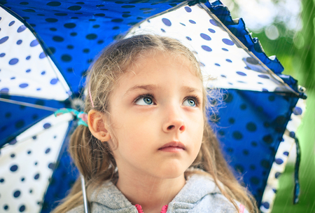 Portrait of a cute sad girl with an umbrella in the rain.の写真素材