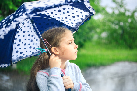 Portrait of a cute sad girl with an umbrella in the rain.の写真素材