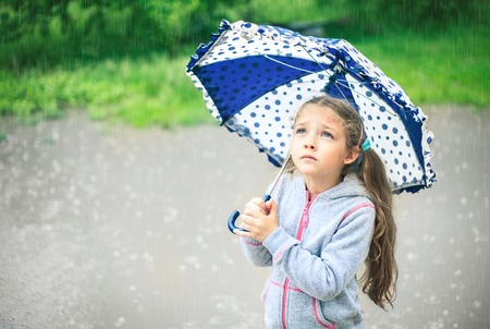 Portrait of a cute sad girl with an umbrella in the rain.の写真素材