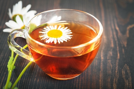 Chamomile tea in a transparent cup closeup, on a wooden table. The concept of herbal medicine.の写真素材