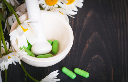 Chamomile flowers and green phytotherapeutic capsules on a wooden table. Herbal medicine and healthの写真素材