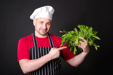 Closeup of happy chef holding arugula beam on black backgroundの写真素材