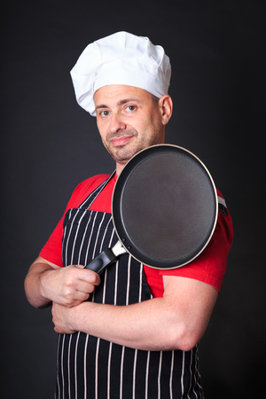 Studio shot of positive chef with a frying pan, over dark background.の写真素材
