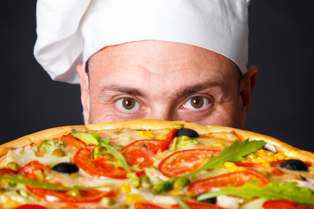 Portrait of happy attractive cook with a pizza in studio an a black backgroundの写真素材