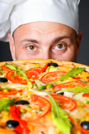 Portrait of happy attractive cook with a pizza in studio an a black backgroundの写真素材
