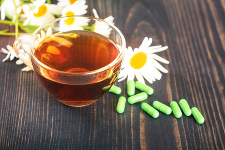 Herbal tea in a transparent cup, capsules and chamomile flowers on wooden table. The concept of alternative medicine and phytotherapy.の写真素材