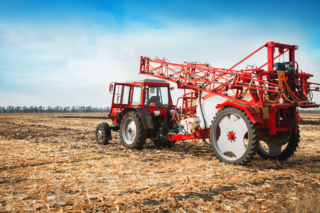 Red tractor with trailed sprayer in a field against a blue sky in a sunny day.の写真素材