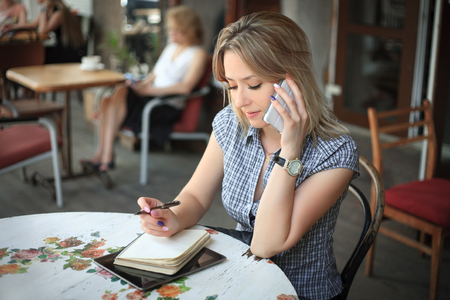 Beautiful woman talking on the phone in a outdoors cafe.の写真素材