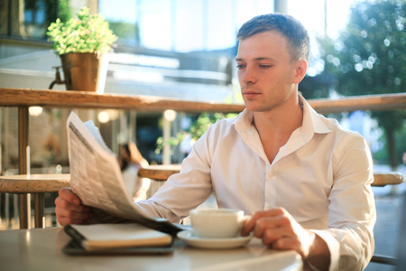 Man is reading a newspaper in a street cafe at lunch.の写真素材