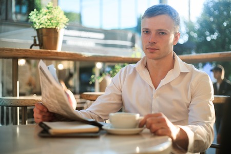 Man is reading a newspaper in a street cafe at lunch looking at the camera.の写真素材