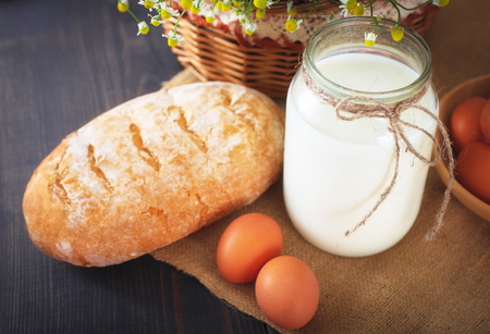 Breakfast from farm products: eggs, milk, fresh bread on a wooden table.の写真素材