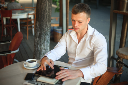Young man drinking coffee and using digital tablet computer in street cafe.の写真素材