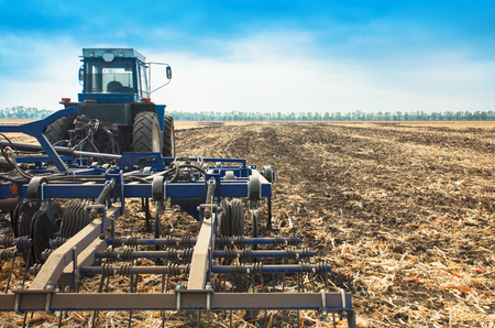 Old blue tractor with a plow in a field on a sunny day. The concept of work in a fields and agriculture industry.の写真素材