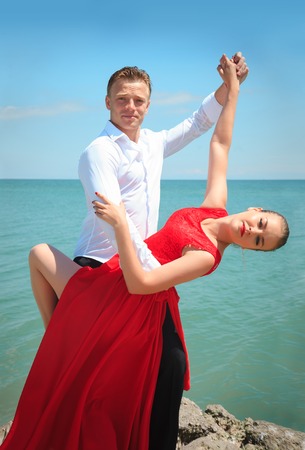 Man and woman posing in dance by the sea on a bright sunny day.の写真素材