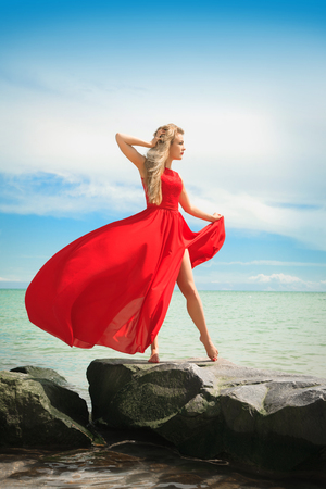 Beautiful woman in a bright red dress by the sea on a sunny summer day.の写真素材