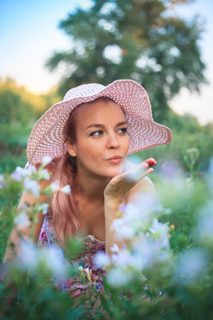 Portrait of a yong woman in a hat on nature in flowers, sends an air kiss.の写真素材