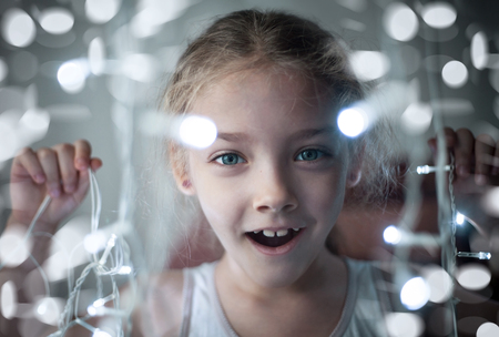 Portrait of a cute preschool girl with a radiant garland of lights in her hands, close up.の写真素材