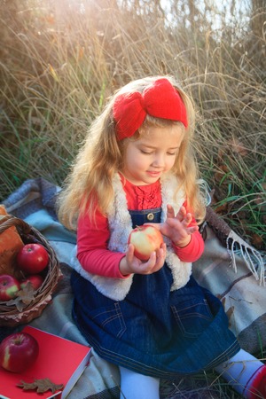Little girl on nature with a basket of fruit and books.の写真素材