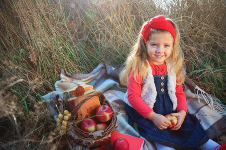 Little girl on nature with a basket of fruit and books.の写真素材
