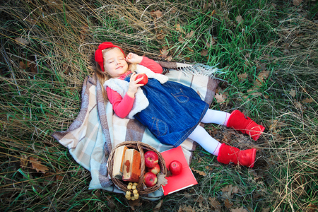 Little girl lying in grass on a plaid with a basket of fruit in the autumn day.の写真素材