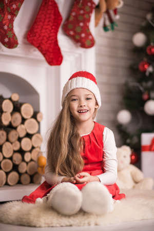 Lovely girl in santa cap sitting on floor in red dress, studio shot, toning in vintage style.の写真素材