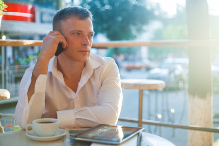 Young man drinking coffee in cafe and using phone. Business people outdoors portrait.の写真素材