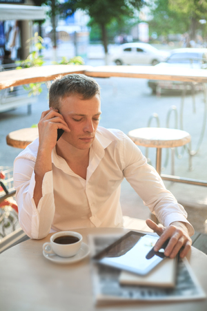 Young man drinking coffee in cafe and using phone. Business people outdoors portrait.の写真素材