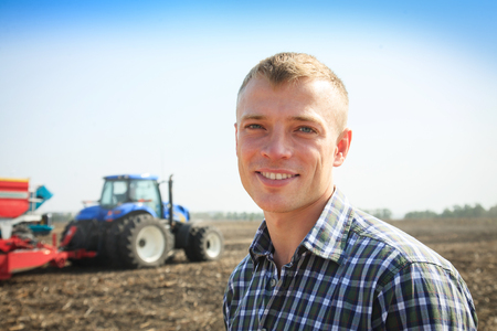 Young attractive man near a tractor. Concept of agriculture and field works.の写真素材