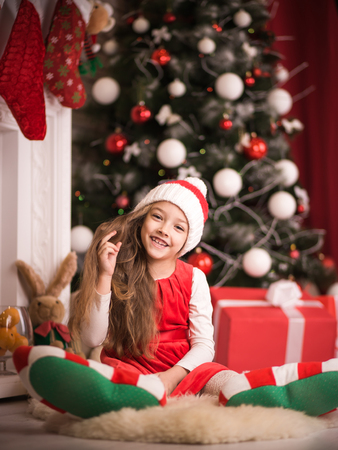 Lovely girl in santa cap lying on floor in red dress, studio shot.の写真素材