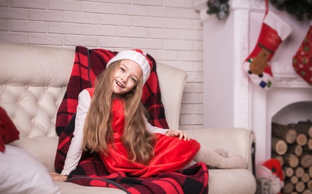 Lovely girl in santa cap lying on a sofa in red dress, studio shotの写真素材