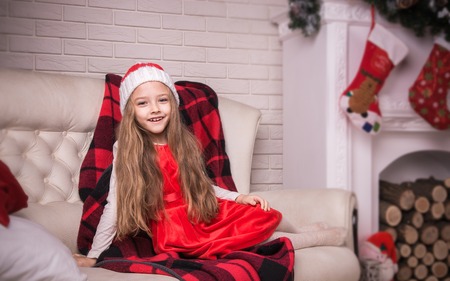 Lovely girl in santa cap lying on a sofa in red dress, studio shotの写真素材
