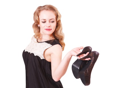 Young cheerful woman in a black short dress and high heels in her hands in the studio on a white backgroundの写真素材