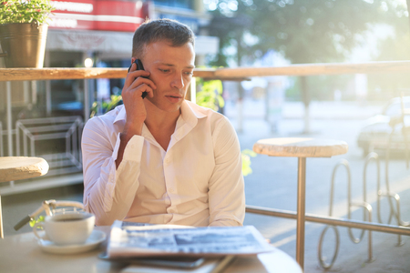 Young man drinking coffee in cafe and using phone. Business people outdoors portrait.の写真素材