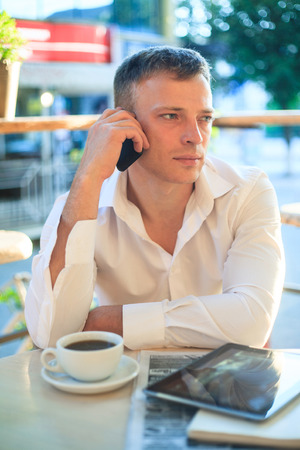Young man drinking coffee in cafe and using phone. Business people outdoors portrait.の写真素材
