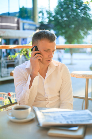 Young man drinking coffee in cafe and using phone. Business people outdoors portrait.の写真素材