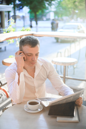 Young man drinking coffee in cafe and using phone. Business people outdoors portrait.の写真素材