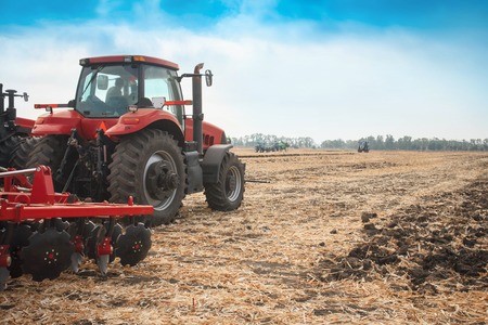 Red tractor working in a field on a bright sunny day. The concept of work in a fields and agriculture industry.の写真素材