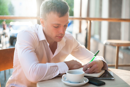 Man writing on notebook or planner with smartphone and coffee on the table at outdoor cafe.の写真素材