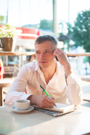 Young man drinking coffee in cafe and using phone. Business people outdoors portrait.の写真素材
