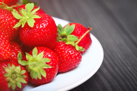 Ripe strawberries in a plate close-up on a wooden table.の写真素材