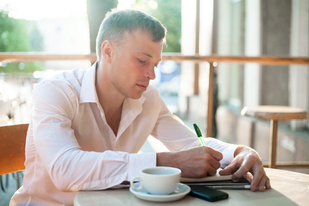 Man writing on notebook or planner with smartphone and coffee on the table at outdoor cafe.の写真素材