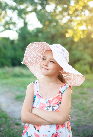 A beautiful school girl in a pink hat in the rays of the sunset on a summer evening in nature outside the city.の写真素材