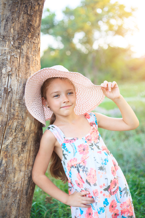 A beautiful school girl in a pink hat in the rays of the sunset on a summer evening in nature outside the city.の写真素材