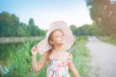A beautiful school girl in a pink hat in the rays of the sunset on a summer evening in nature outside the city.の写真素材
