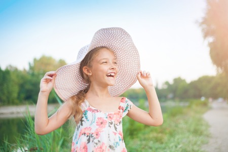 A beautiful girl in a pink hat in the rays of the sunset on a summer evening in nature outside the city.の写真素材