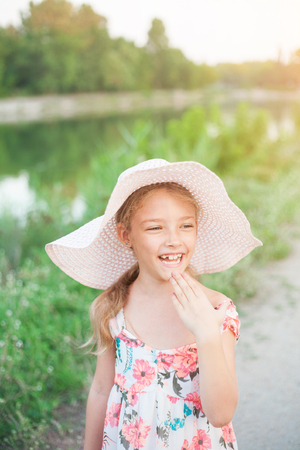 A beautiful girl in a pink hat in the rays of the sunset on a summer evening in nature outside the city.の写真素材