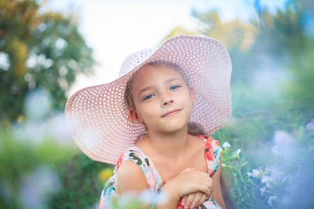 Beautiful girl in a pink hat in summer in a green garden among flowers.の写真素材